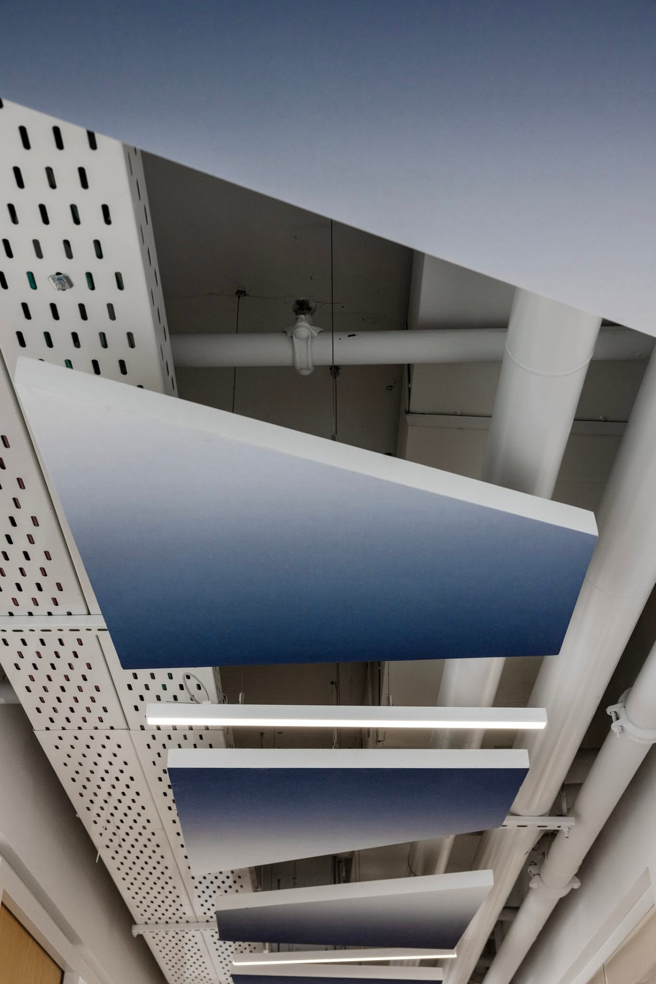 Ceiling rafts — gradient panels cut on an angle and hung off the service grid.